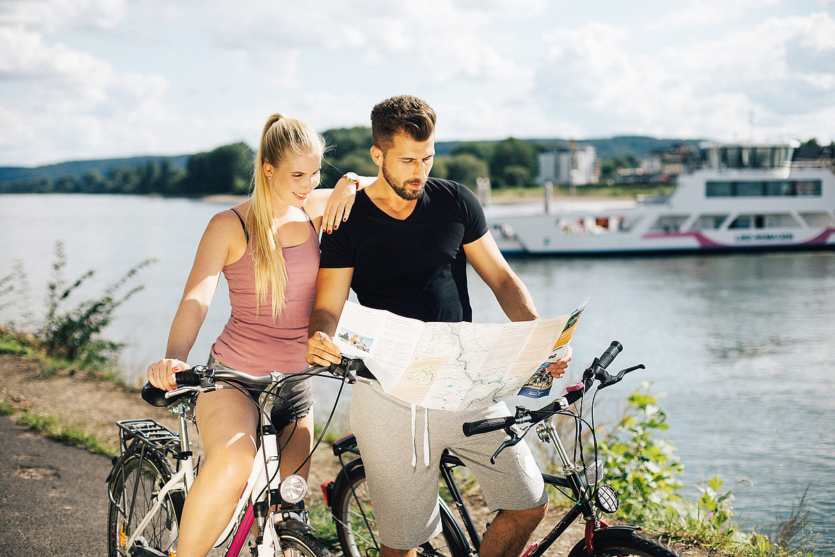 Junges Pärchen auf Rädern im Sonnenschein am Rhein die eine Radkarte lesen